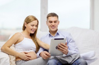 Un couple heureux regarde une tablette. Une des deux personnes est enceinte